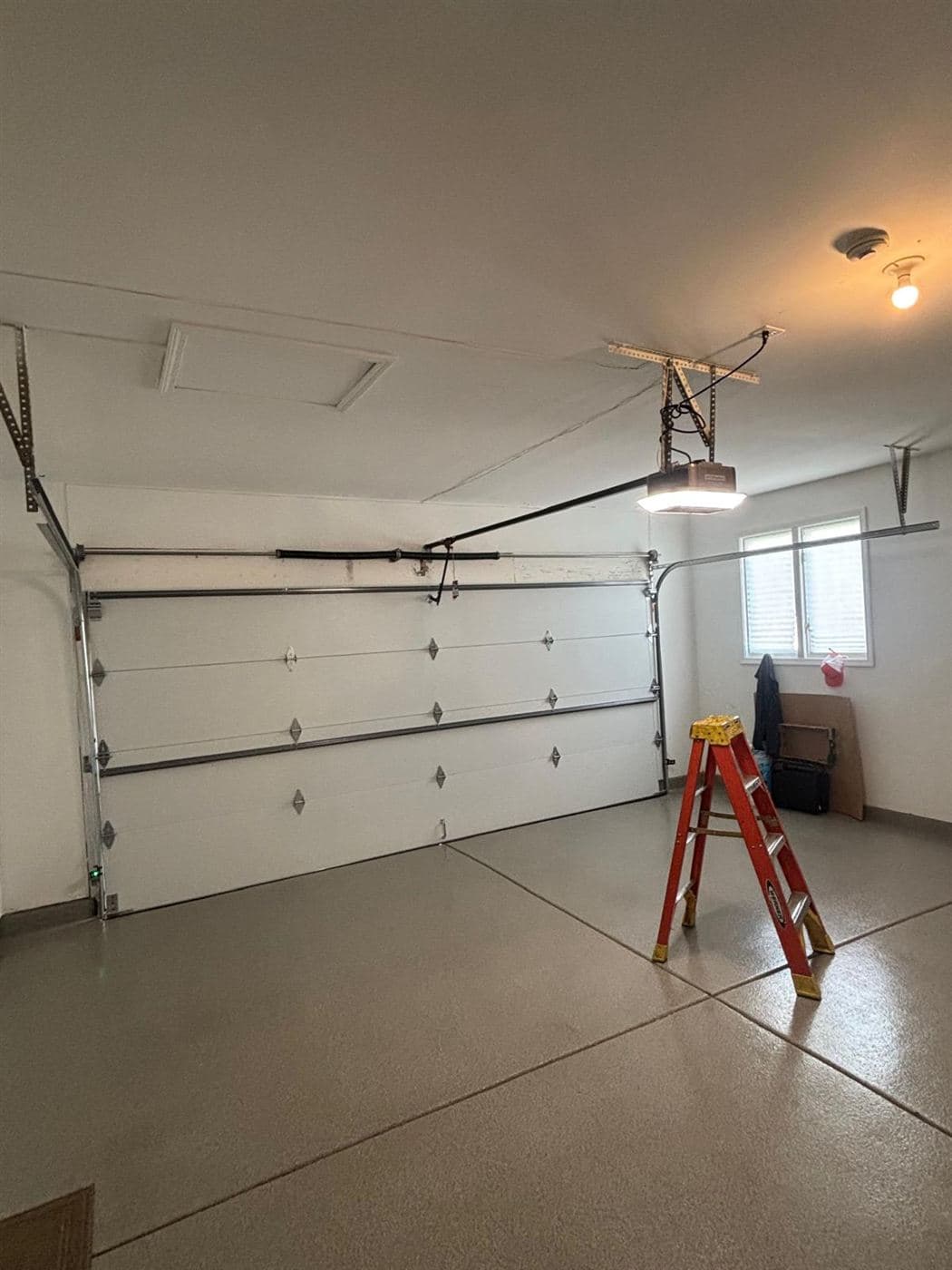 Garage interior with a ladder set up under a sectional door and opener rail