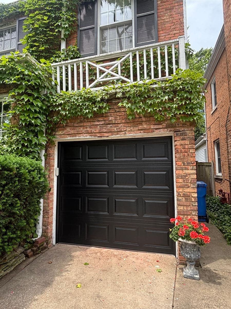 Black paneled garage door in a brick arch covered in ivy