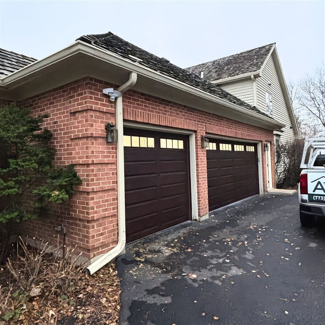 Two dark brown garage doors on a brick home