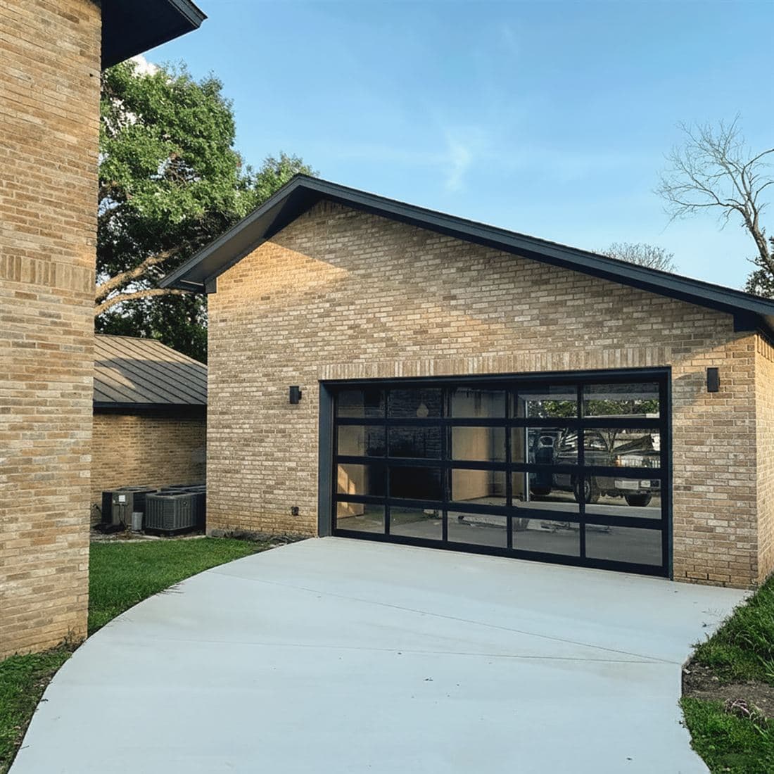 Modern full-view glass garage door on a brick garage